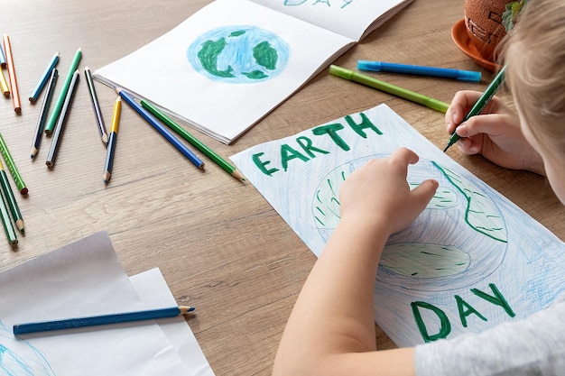 Een kind thuis aan tafel tekent de planeet aarde met een wereldkaart met veelkleurige potloden