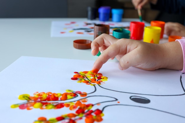 Een kind trekt bladeren aan een boom Ideeën voor het tekenen met vingerverven Vingerverven voor kinderen op witte achtergrond Klein meisje schilderen door vinger handverfkleur Kinderen ontwikkelingsconcept