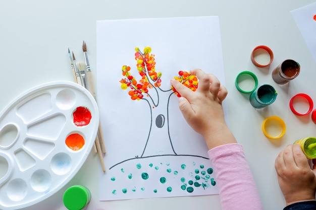 Een kind trekt bladeren aan een boom Ideeën voor het tekenen met vingerverven Vingerverven voor kinderen op witte achtergrond Klein meisje schilderen door vinger handverfkleur Kinderen ontwikkelingsconcept