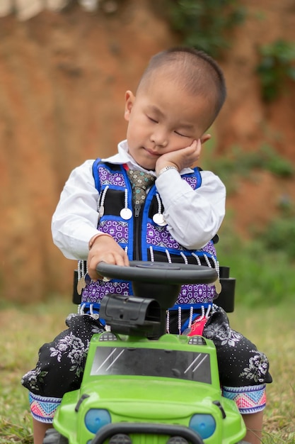 Een kind zit op zijn groene speelgoedauto en poseert als een traditionele slaapkleding