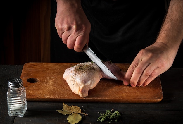 Een kippenpoot koken met de handen van een chef-kok op een donkere achtergrond.