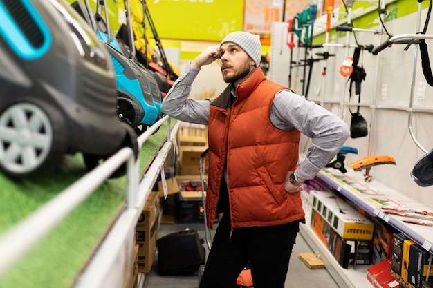 Een klant in een tuinwinkel kiest tussen een benzine- of elektrische grasmaaier