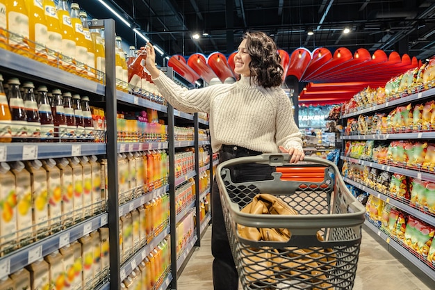Een klant kiest een fles sap uit de schappen van de supermarkt terwijl ze haar karretje manoeuvreert