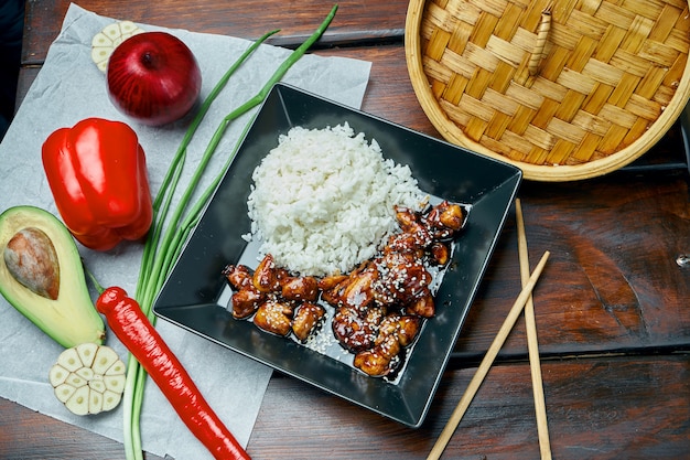 Een klassieke Aziatische gerecht - rijst met teriyaki gebakken varkensvlees wok in een zwarte plaat op een houten tafel. Detailopname