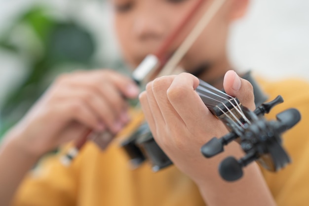 Een klein Aziatisch kind speelt en oefent viool muzikaal snaarinstrument tegen thuis