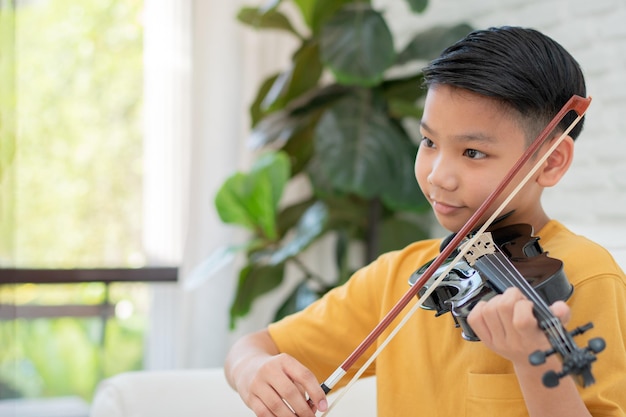 Een klein Aziatisch kind speelt en oefent viool muzikaal snaarinstrument tegen thuis