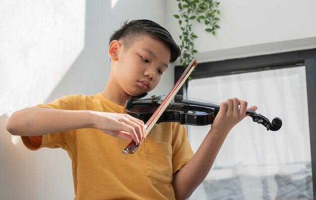 Een klein Aziatisch kind speelt en oefent viool muzikaal snaarinstrument tegen thuis