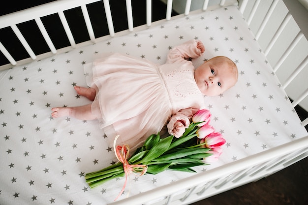 Een klein babymeisje liggend op een bed met een boeket roze tulpen. Een cadeau voor mama voor een vakantie.