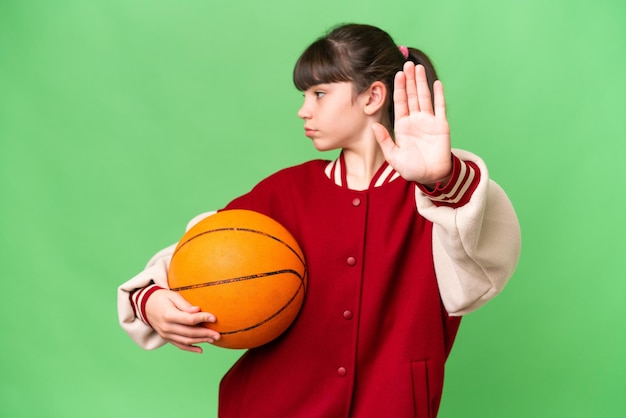 Een klein blank meisje dat basketbal speelt over een geïsoleerde achtergrond en een stopgebaar maakt en teleurgesteld is