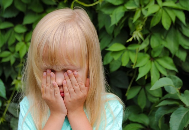 Een klein blond meisje huilt bedekt haar gezicht met haar handen voelt emoties van verdriet