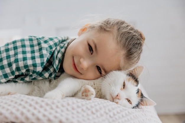 Een klein blond meisje in een pyjama knuffelt een huiskat in haar slaapkamer het concept van een gezellige thuismorgen