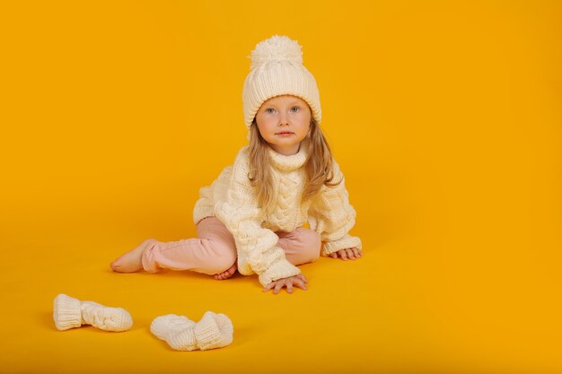 een klein blond meisje in een witte gebreide trui, muts en sokken