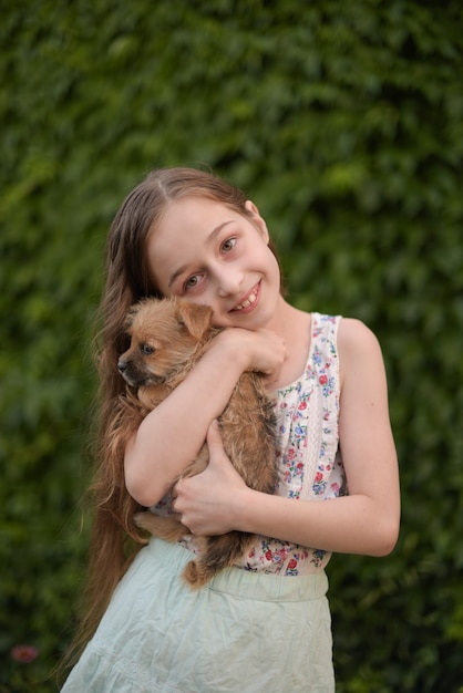 Een klein blond meisje met haar huisdierenhond outdooors in park. Het meisje houdt van een kleine puppy.