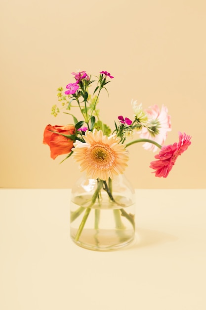 Een klein boeket lentebloemen in een glazen vaas tegen een gele achtergrond. Zomer lay-out met kopie ruimte.