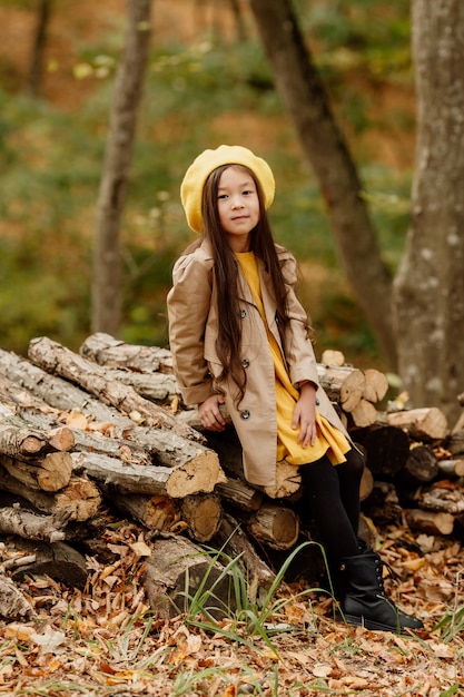 Een klein brunette Aziatisch meisje in herfstkleren loopt in het herfstbos bij een beekje