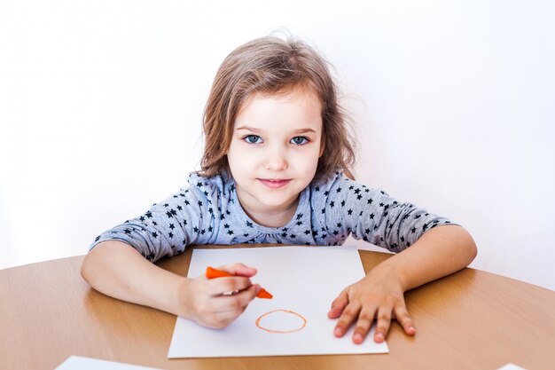 Een klein en schattig meisje zit aan een tafel en tekent