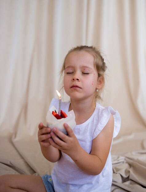 Een klein feestvarken houdt een cupcake met een kaars vast en doet een wens op een beige achtergrond met een plek voor tekst