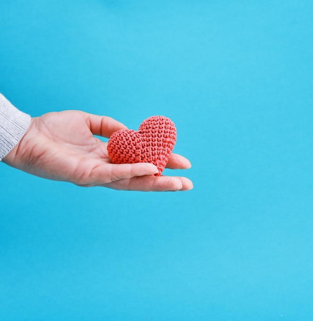 Een klein gebreid rood hart in een menselijke hand