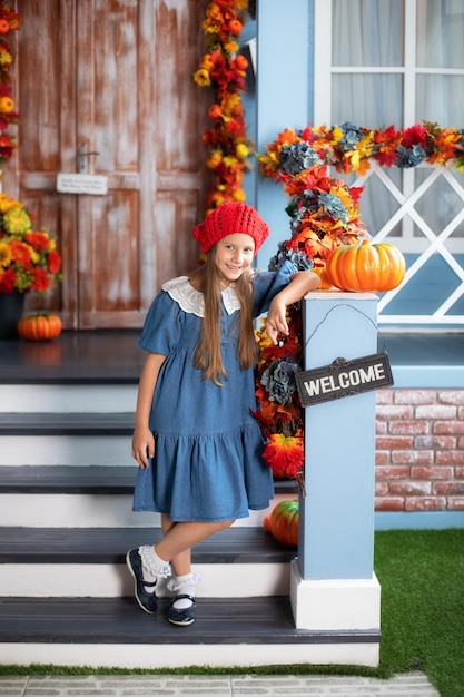 Een klein glimlachend gelukkig meisje staat met pompoen op de veranda van het huis op Halloween.