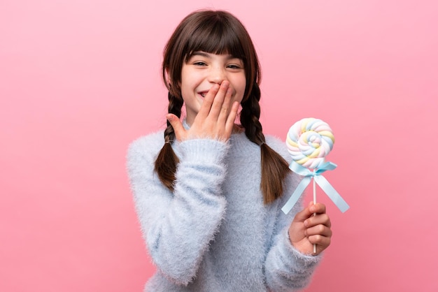 Een klein kaukasisch meisje met een lolly blij en glimlachend die de mond bedekt met de hand