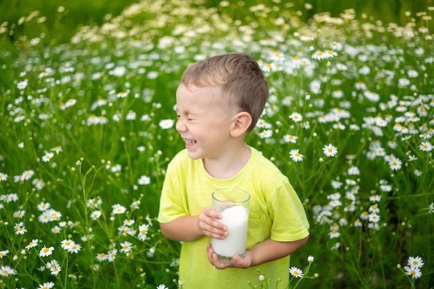 Een klein kind een jongen in kleding gemaakt van natuurlijk katoen loopt over het veld met een glas melk in zijn handen geniet van het leven geniet van de natuur