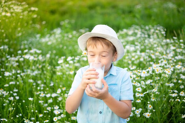 Een klein kind een jongen met een hoed loopt over het veld met een glas melk in zijn handen