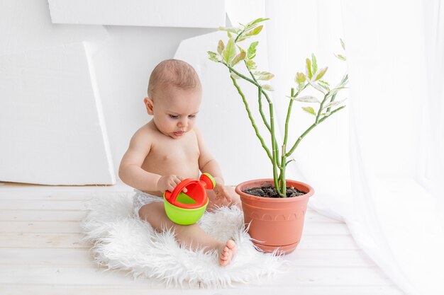 Een klein kind een jongen van 8 maanden zit bij een plant met een gieter