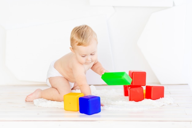 Een klein kind, een jongen van zes maanden, speelt met heldere blokjes in een helderwitte kamer in luiers