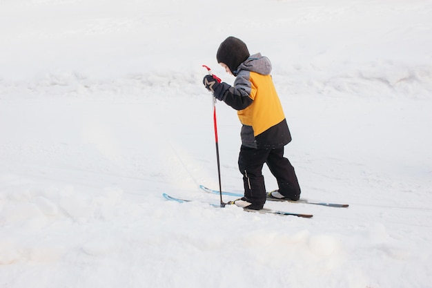 Een klein kind in een gele jas langlaufen in de sneeuw Wintersport Een kind leert skiën