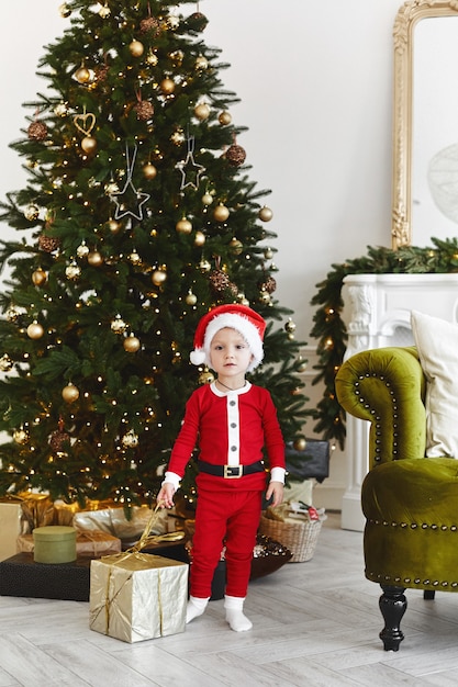 Een klein kind in een kerstman kostuum poseren met een kerstcadeau doos in de buurt van de kerstboom