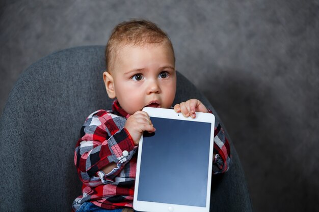 Een klein kind in een overhemd knaagt aan een tablet