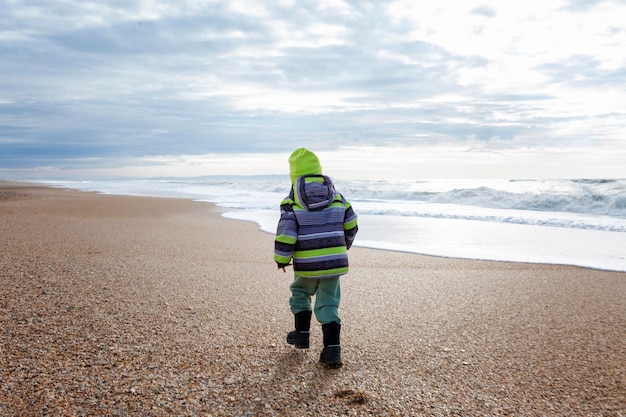 Een klein kind in warme kleren loopt langs de kust tijdens het koude seizoen activiteit en wandelingen