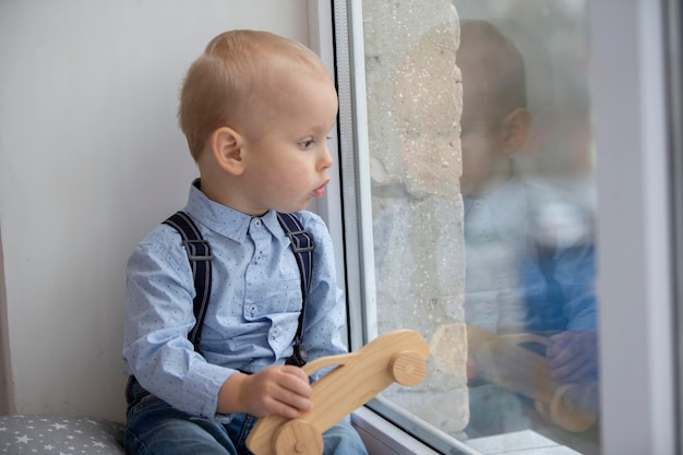 Een klein kind kijkt uit het raam Het kind met speelgoed zit op een vensterbank