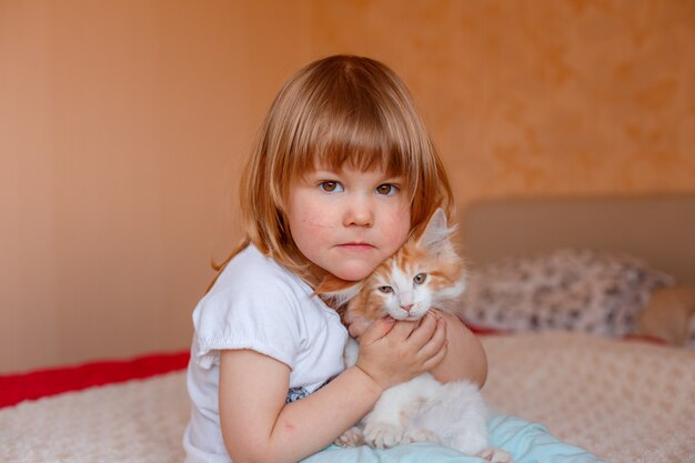 een klein kind knuffelt een roodharige kitten in de slaapkamer