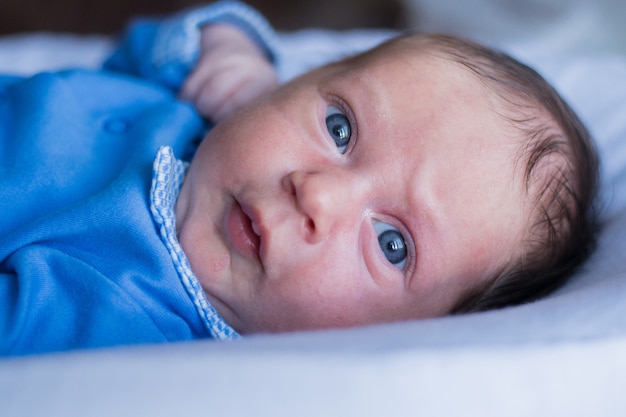 Een klein kind met blauwe ogen kijkt verbaasd in de camera met fronsende wenkbrauwen in een blauwe blouse h...