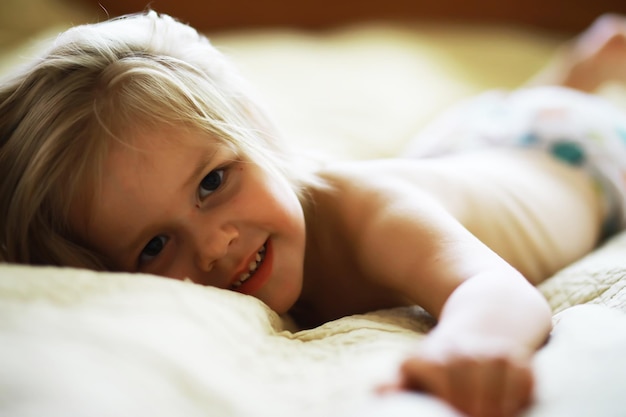 Een klein kind met blond haar ligt op het bed Babymeisje speelt op de bank