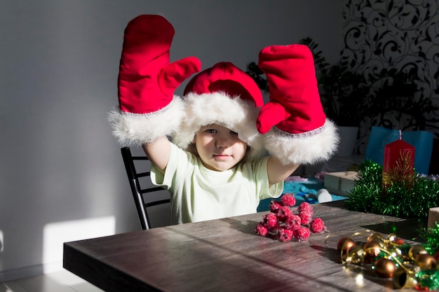 Een klein kind met een kerstmuts en rode wanten met kerstcadeaus zit aan de nieuwjaarstafel