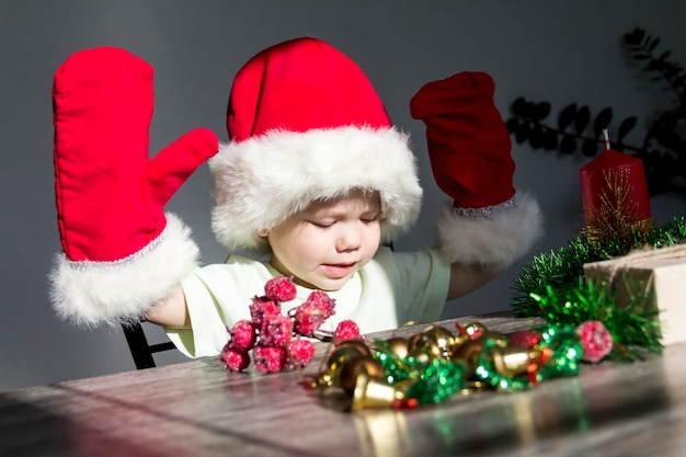 Een klein kind met een kerstmuts en rode wanten met kerstcadeaus zit aan de nieuwjaarstafel