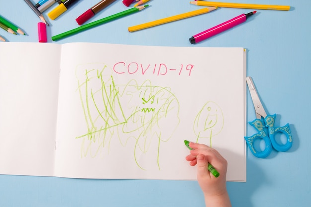 Een klein kind tekent groen waskrijt in een album