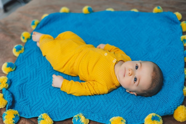 Een klein kind van 45 maanden oud ligt op een bed in gele kleren Het kind begint zijn hoofd vast te houden Babykleding