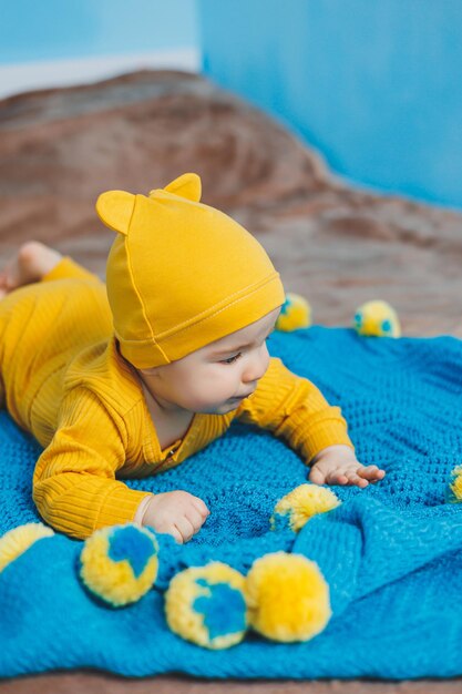 Een klein kind van 45 maanden oud ligt op een bed in gele kleren Het kind begint zijn hoofd vast te houden Babykleding