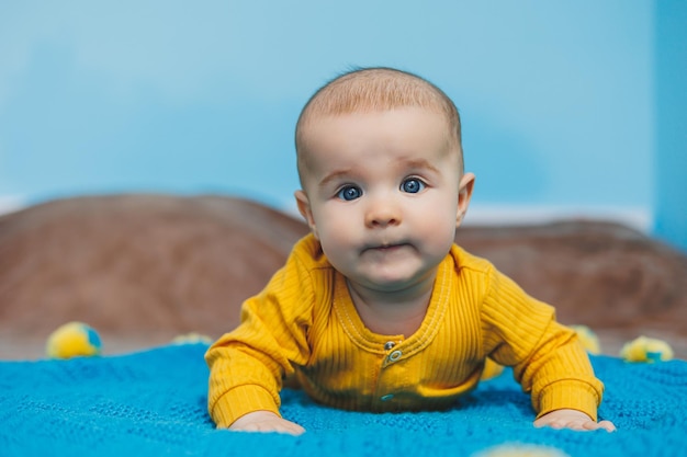 Een klein kind van 45 maanden oud ligt op een bed in gele kleren Het kind begint zijn hoofd vast te houden Babykleding