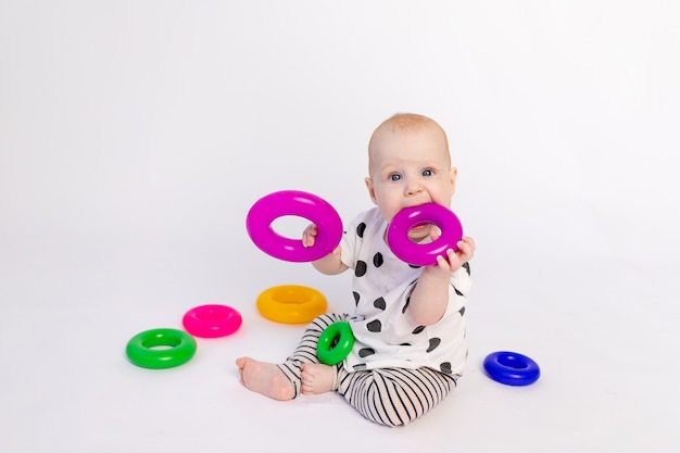 Een klein kind van 8 maanden kauwt speelgoed op een witte geïsoleerde achtergrond, vroege ontwikkeling van kinderen tot een jaar, plaats voor tekst