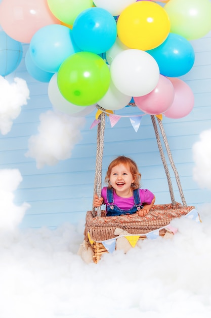 Een klein kind vliegt op een bundel gekleurde ballonnen gevuld met helium en staat in een houten pilootmand. gelegen in de lucht tussen de wolken. hemel decoratie