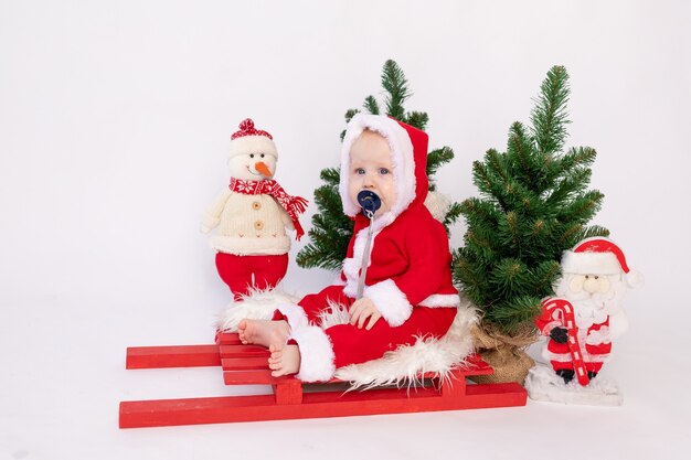 Een klein kind zit in de mand van de kerstman op een witte achtergrond geïsoleerd in een hoed en met kerstbomen, een plek voor tekst