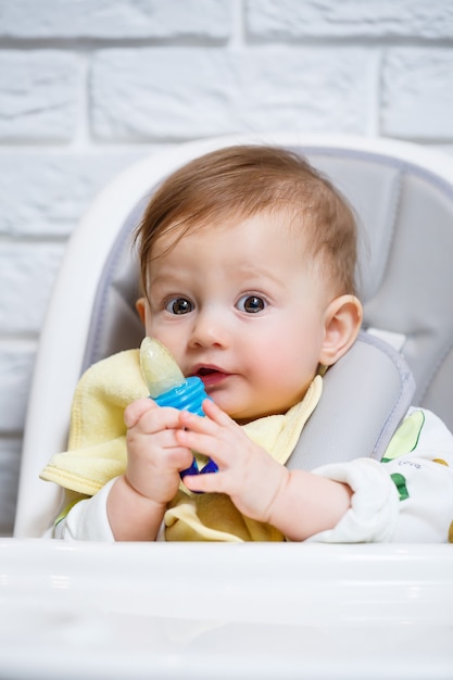 Een klein kind zit op een hoge stoel en eet fruit via het net. Knabbelschaar voor het voeden van baby's