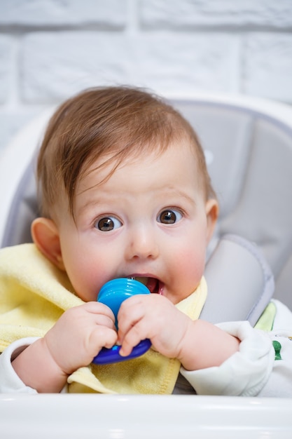 Een klein kind zit op een hoge stoel en eet fruit via het net. knabbelschaar voor het voeden van baby's