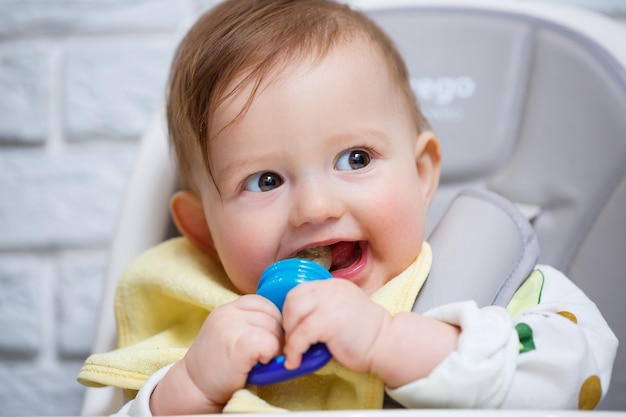 Een klein kind zit op een hoge stoel en eet fruit via het net. Knabbelschaar voor het voeden van baby's