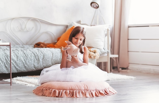 Een klein lachend schattig meisje in een mooie witte jurk zit met een zacht stuk speelgoed in haar handen