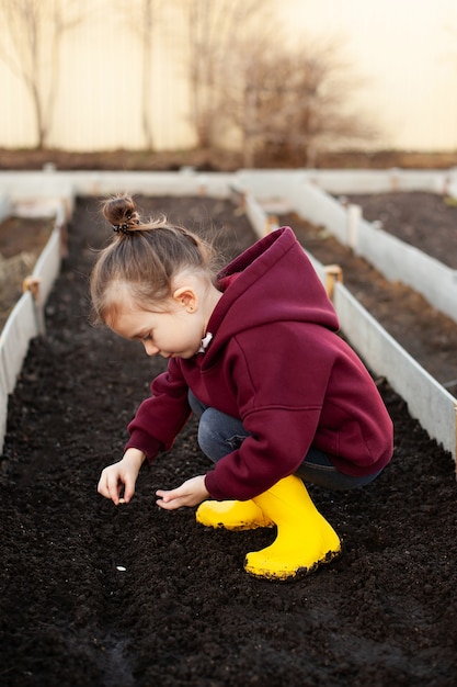 Een klein lief meisje in gele laarzen plant zaden van groenten en bloemen op het bed